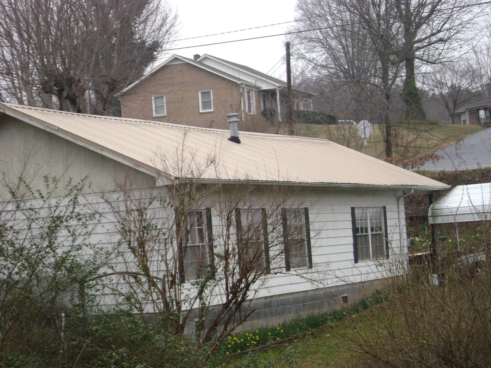 Tan metal roof on a white sided house set into a hillside — Commercial Roofing by Roofing Brothers in Lakeland
